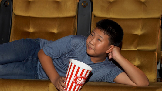 男孩躺着看电影开心地吃爆米花在电影院享受图片