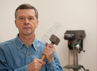 在一个家庭工作间中男子在面对照相机并举着大块锤子的家庭工作间中图片
