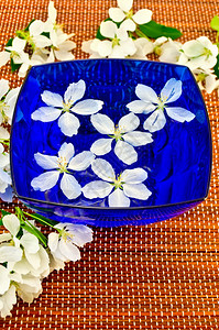 蓝色杯子里白苹果树的花加上水和棕竹垫图片