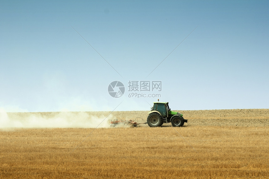 蓝色天空背景的拖拉机犁田图片