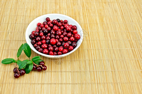 白瓷碗里的林边莓两根树枝加浆果和竹垫上的绿叶子图片
