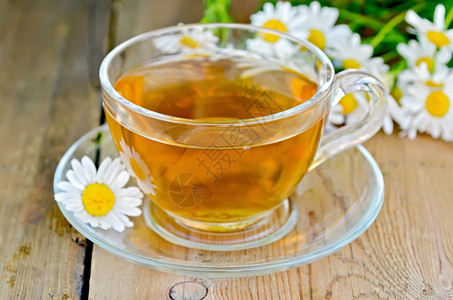 玻璃杯中的草药茶木板背景上鲜的甘菊花图片
