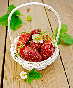 熟的红草莓有叶子和花朵放在本底木板上的白圆篮子图片