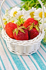 红色草莓在白圆篮子中一束香菊花背景是绿条餐巾纸图片
