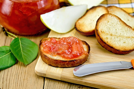 烤面包片一个加梨果酱的玻璃罐背景木板上的刀图片