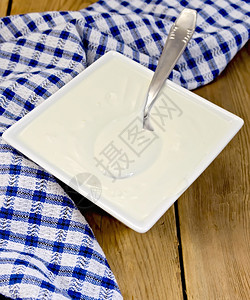 白方碗中的酸奶油蓝彩餐巾纸木板上的勺子图片