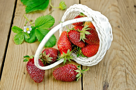 从白圆篮子鲜花和草莓叶上浇灌的成熟红草莓木板底图片