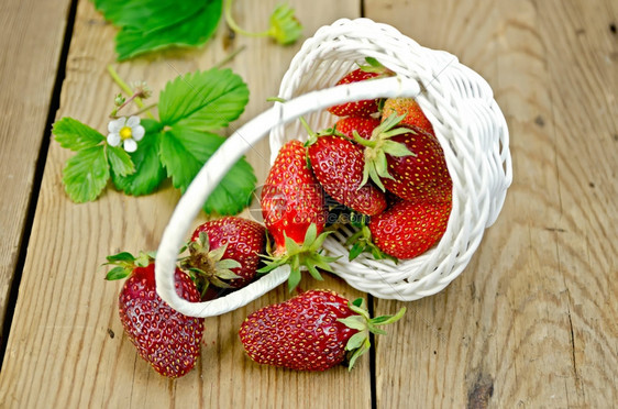 从白圆篮子鲜花和草莓叶上浇灌的成熟红草莓木板底图片