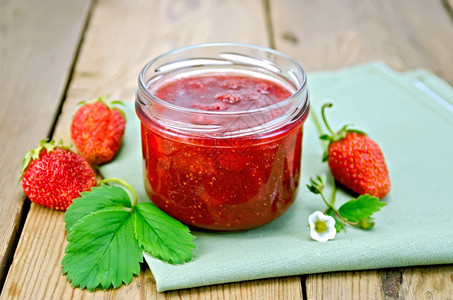 玻璃罐中的草莓果酱叶子和花草莓木板背景上的餐巾纸图片