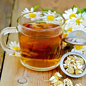 茶杯中的金属筛子含干甘菊花木板背景上的一束鲜花朵图片