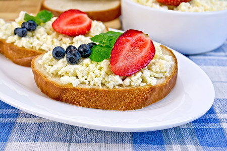 一片面包粉薄蓝莓和草一碗干酪在蓝色桌布背景的板上面包图片