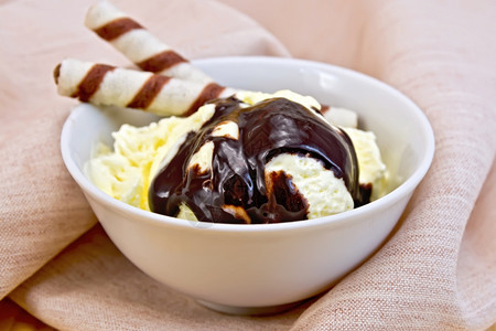 一碗香草冰淇淋里有面包卷和巧克力糖浆放在木板背景的餐巾纸上图片