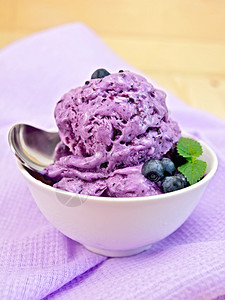 蓝莓冰淇淋夹薄荷叶碗里有浆果薄荷和勺子底有紫布和木板图片