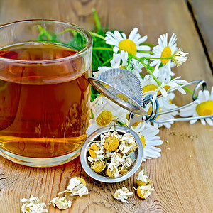 含干甘菊花的金属筛子一束香菊鲜花的束木板背景上的玻璃杯茶图片