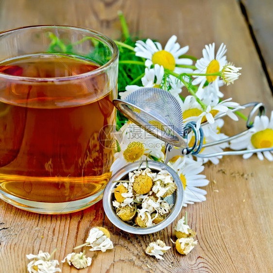 含干甘菊花的金属筛子一束香菊鲜花的束木板背景上的玻璃杯茶图片