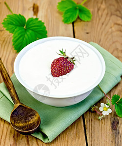 厚的酸奶碗里有草莓餐巾纸上有勺子木板草莓树叶和鲜花图片