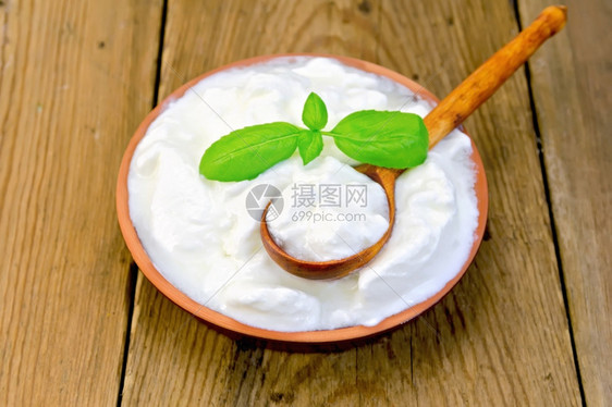厚的酸奶在粘土碗中木板背景上用烤肉和勺子做面粉图片