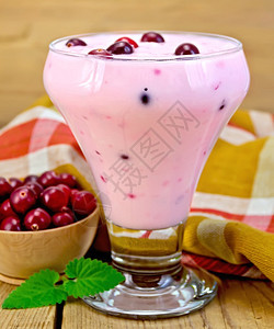 一杯子的厚酸奶配有红莓勺子餐巾碗中的红莓木板上薄荷图片