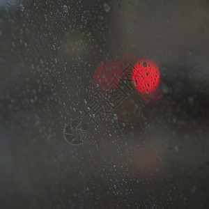 降雨时通过湿挡风玻璃看见的红色交通灯图片