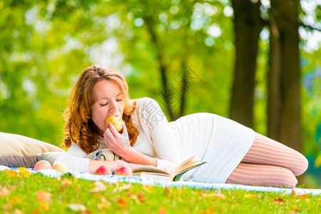 女人周末在公园休息吃着苹果看书图片