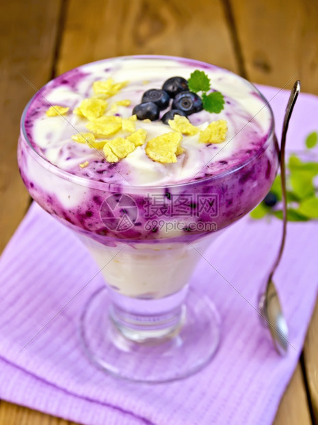用蓝莓玉米片卷饼勺子和的甜牛奶放在木板背景的紫色餐巾纸上玻璃具图片