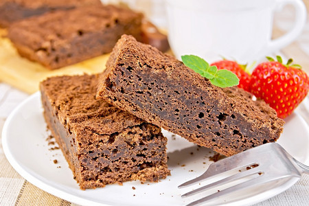 两块巧克力蛋糕放在盘子上草莓和薄荷放在叉子上图片