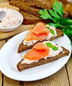 两块三边的黑麦面包上三明治奶油巴西尔和鲑鱼刀餐巾木板上的面条图片