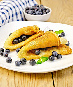 两煎饼蓝莓和白盘薄荷餐巾纸木板上浆果碗图片