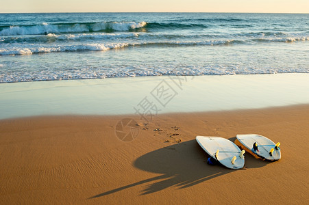 日落时在海滩上躺着两个冲浪板图片