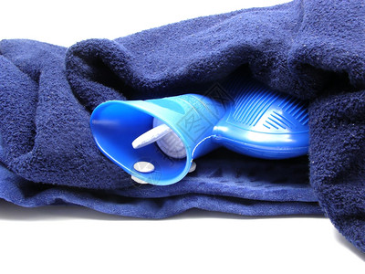 蓝色热水袋包裹在白色背景的蓝毯子中图片