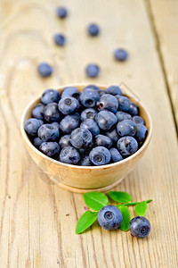 木碗中的蓝莓绿叶树枝和木板上浆果图片