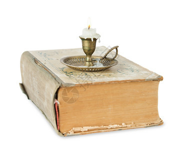 在黄铜蜡烛台上烧站在白色背景上被孤立的旧厚书上背景图片