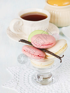 五颜六色的杏仁饼放在一个圆形花边餐巾和一杯茶上的玻璃冰淇淋碗里图片