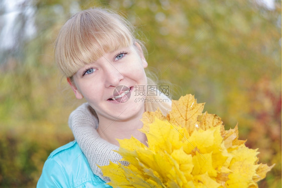 一个微笑的年轻女孩肖像在秋天带着黄色的木叶花束看着镜头图片