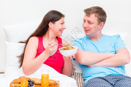 快乐的年轻夫妇一起在床上吃早餐图片
