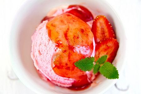 白碗中草莓冰淇淋上面有草莓薄荷和糖浆放在底浅木板上图片