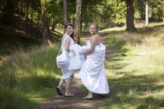两个新娘在森林道路上抱着裙子走图片
