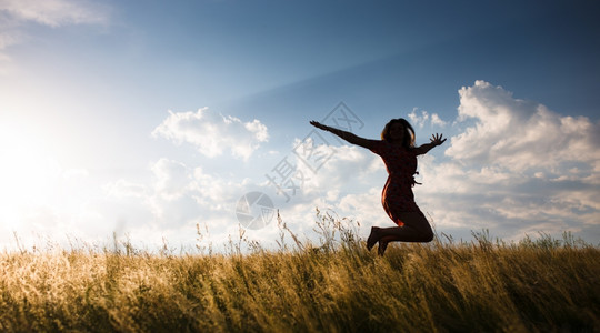 日落时女子在草地上跳跃图片