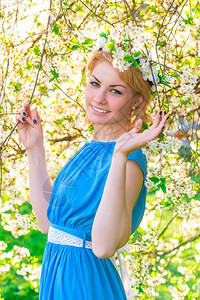 美丽的金发女穿着蓝色的裙子在花樱桃的树枝图片