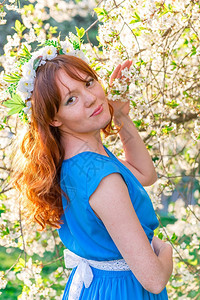 穿着蓝裙子的红头发女孩春天在开花樱桃附近图片
