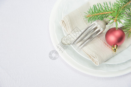 白色瓷板上摆着白色桌布上面是白色桌布的子上面是白色的瓷板上面是旧刀叉红色的圣诞节球和绿色的树枝图片