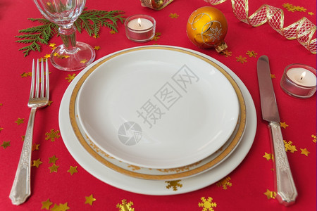银刀叉子餐盘酒杯和燃烧蜡烛放在一张桌子上面有红色桌布图片