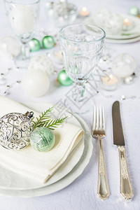 白瓷板上摆着桌布的瓷板盘子上摆着白桌布面板上摆着白桌布面有刀和叉子美丽的酒杯和绿色圣诞节球图片