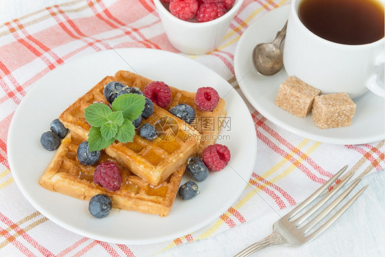 美味的早餐甜华芙饼草莓蓝和一杯咖啡放在餐巾纸上的图片