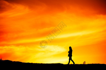 一个孤单的女人在日落时山上行走图片