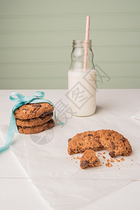 巧克力曲奇饼带蓝丝和一杯牛奶根稻草在白木桌上图片