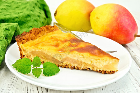 一块梨饼白盘上加奶油酱叉子梨和薄荷木板上的餐巾纸图片