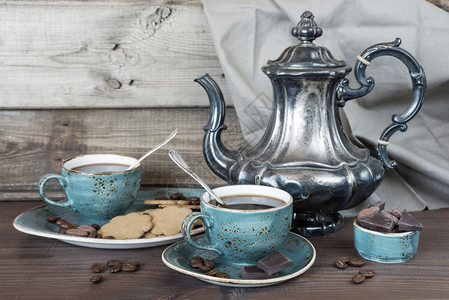 蓝色古董杯饼干巧克力和古董银咖啡壶中的黑旧木板图片