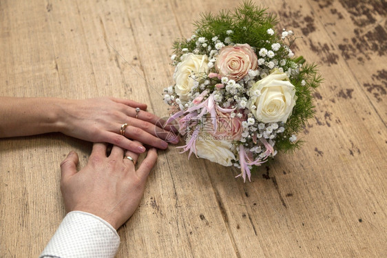 新娘和郎的手结婚戒指在木桌上玫瑰花束图片