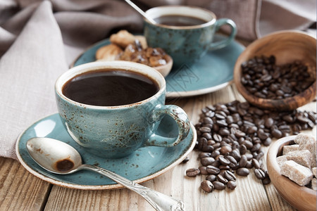 两杯蓝色黑咖啡木碗中的糖块和布底上分散的咖啡豆图片